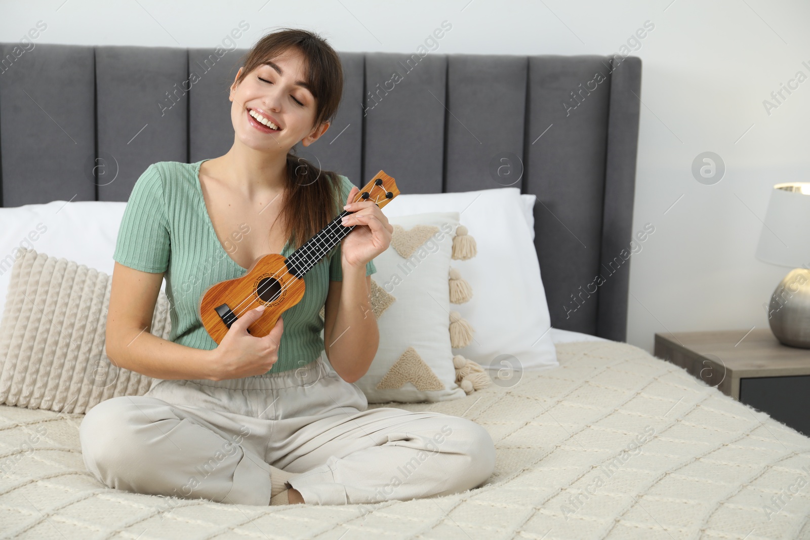 Photo of Happy woman playing ukulele on bed at home