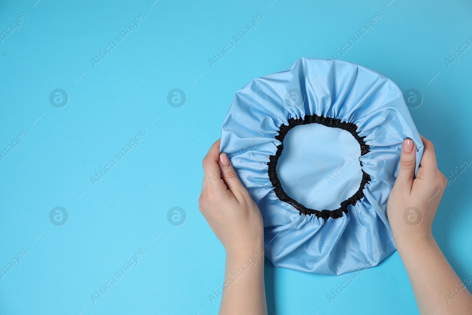 Photo of Woman with shower cap on light blue background, top view. Space for text