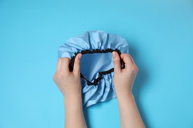 Photo of Woman with shower cap on light blue background, top view