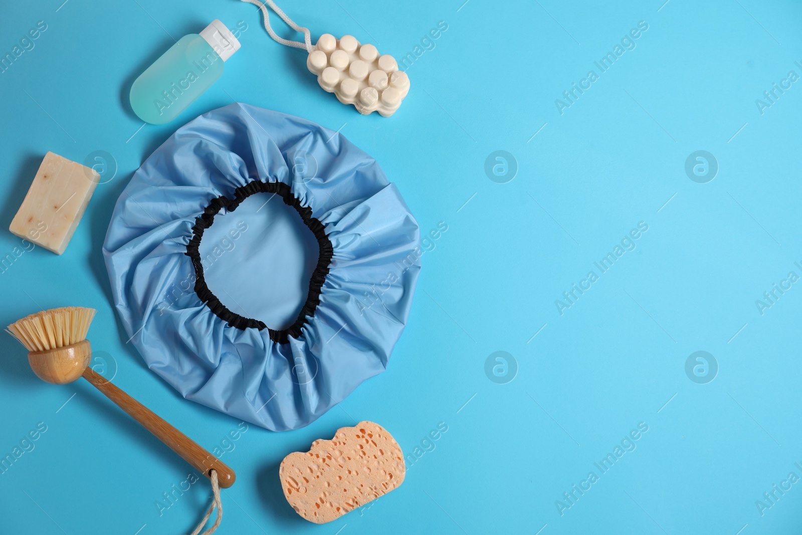 Photo of Shower cap and bath accessories on light blue background, flat lay. Space for text