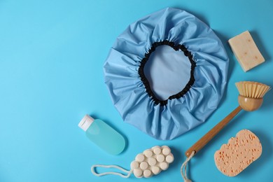 Photo of Shower cap and bath accessories on light blue background, flat lay. Space for text