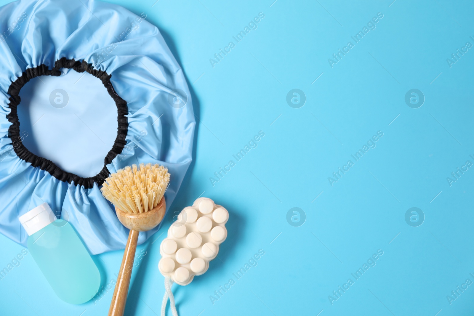 Photo of Shower cap and bath accessories on light blue background, flat lay. Space for text