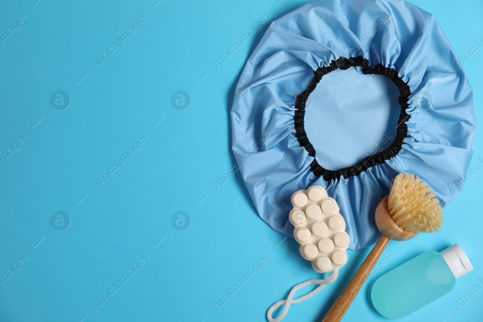 Photo of Shower cap and bath accessories on light blue background, flat lay. Space for text