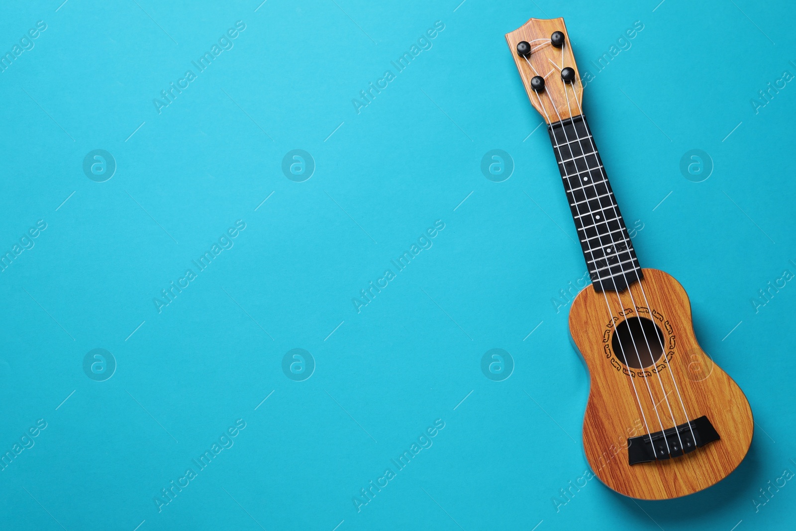 Photo of One ukulele on light blue background, top view. Space for text