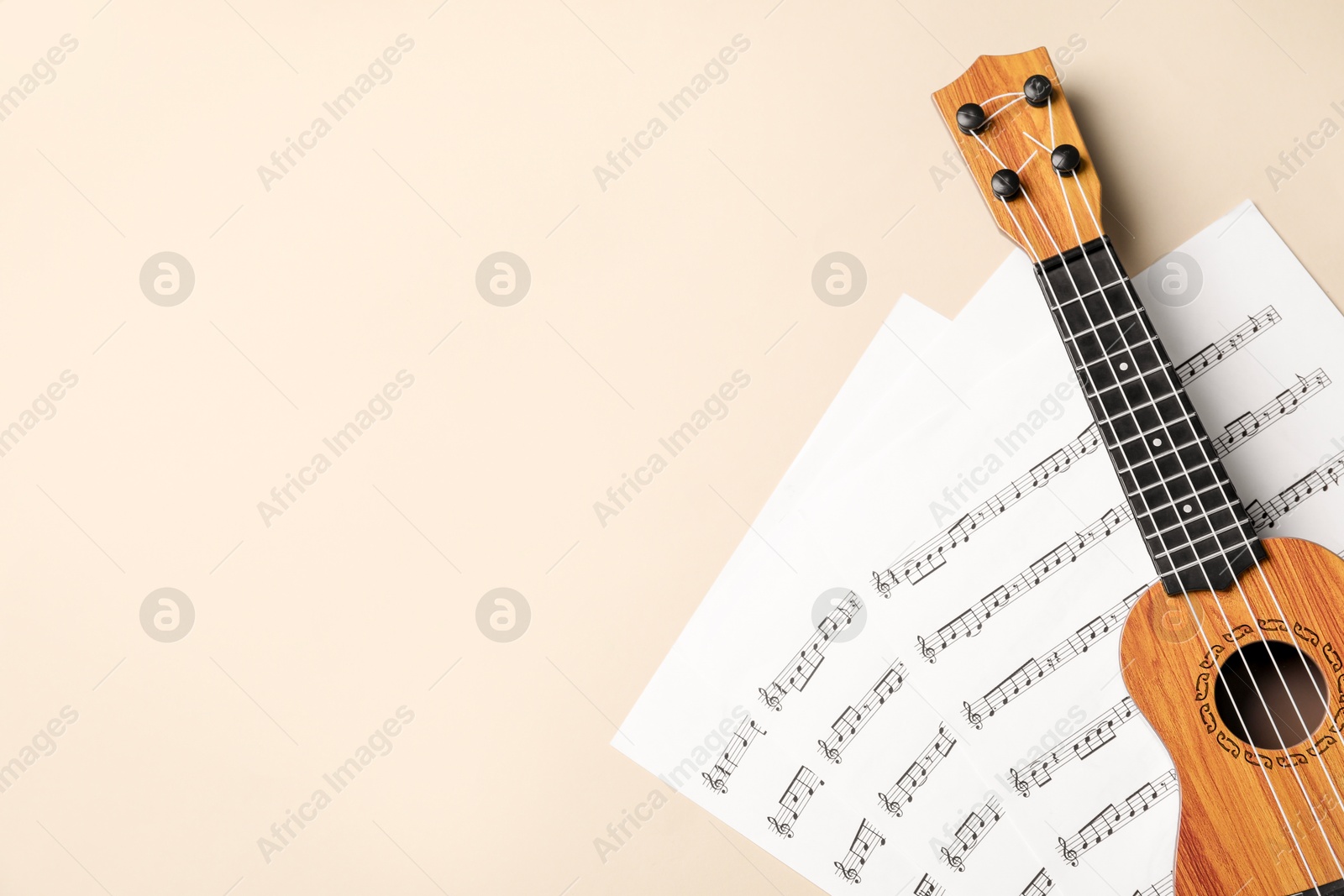 Photo of Ukulele and music sheets on beige background, top view. Space for text