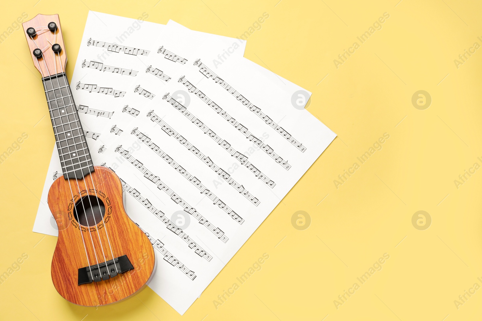 Photo of Ukulele and music sheets on yellow background, top view. Space for text