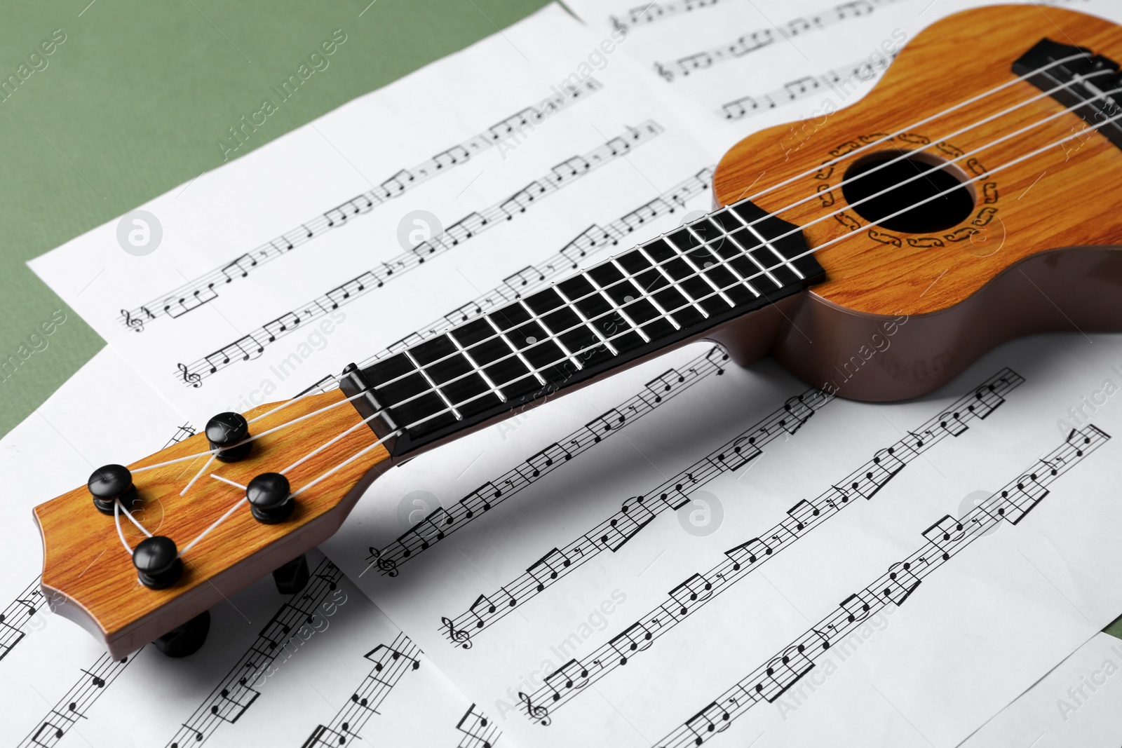 Photo of Ukulele and music sheets on green background, closeup