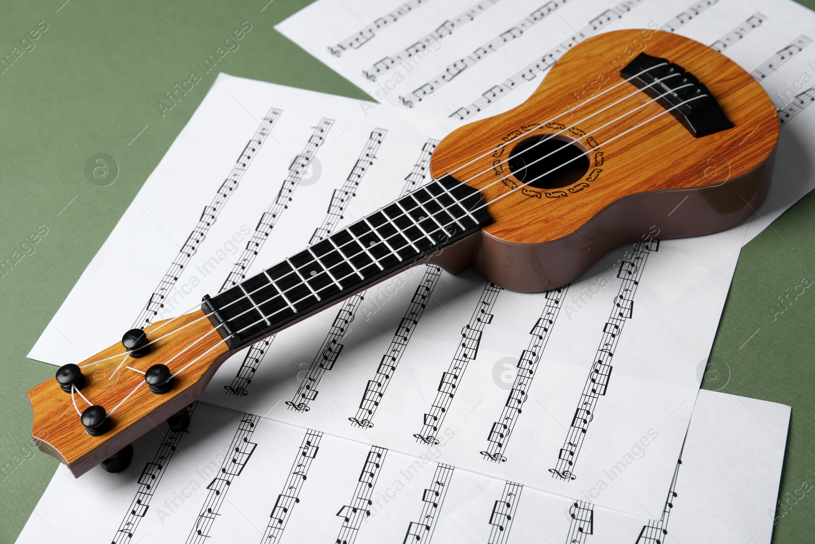 Photo of Ukulele and music sheets on green background, closeup