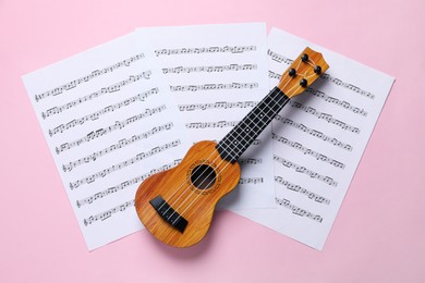 Photo of Ukulele and music sheets on pink background, top view