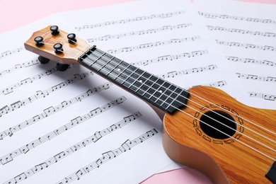 Photo of Ukulele and music sheets on pink background, closeup