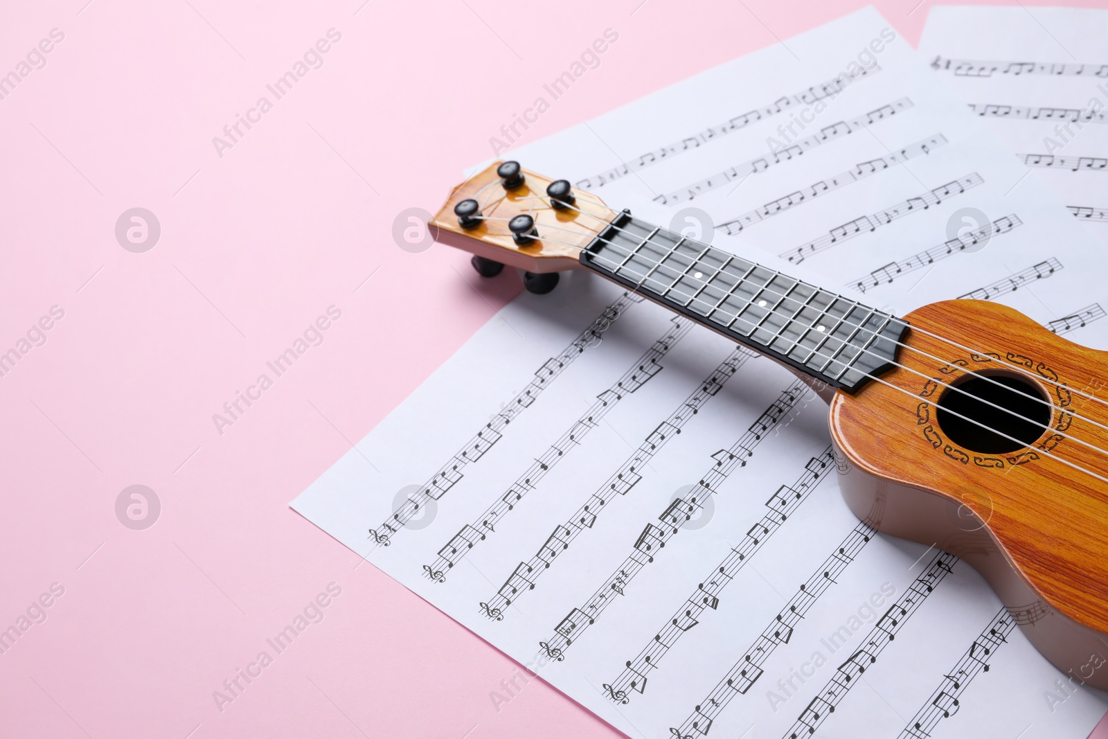 Photo of Ukulele and music sheets on pink background, space for text