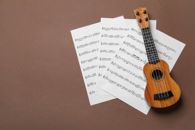 Photo of Ukulele and music sheets on brown background, top view. Space for text