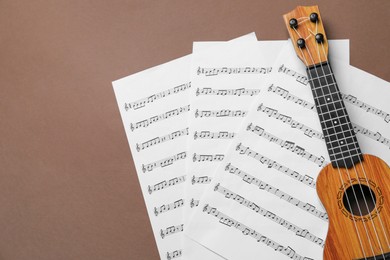 Photo of Ukulele and music sheets on brown background, top view. Space for text