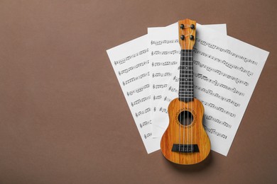 Photo of Ukulele and music sheets on brown background, top view. Space for text