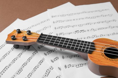 Photo of Ukulele and music sheets on brown background, closeup