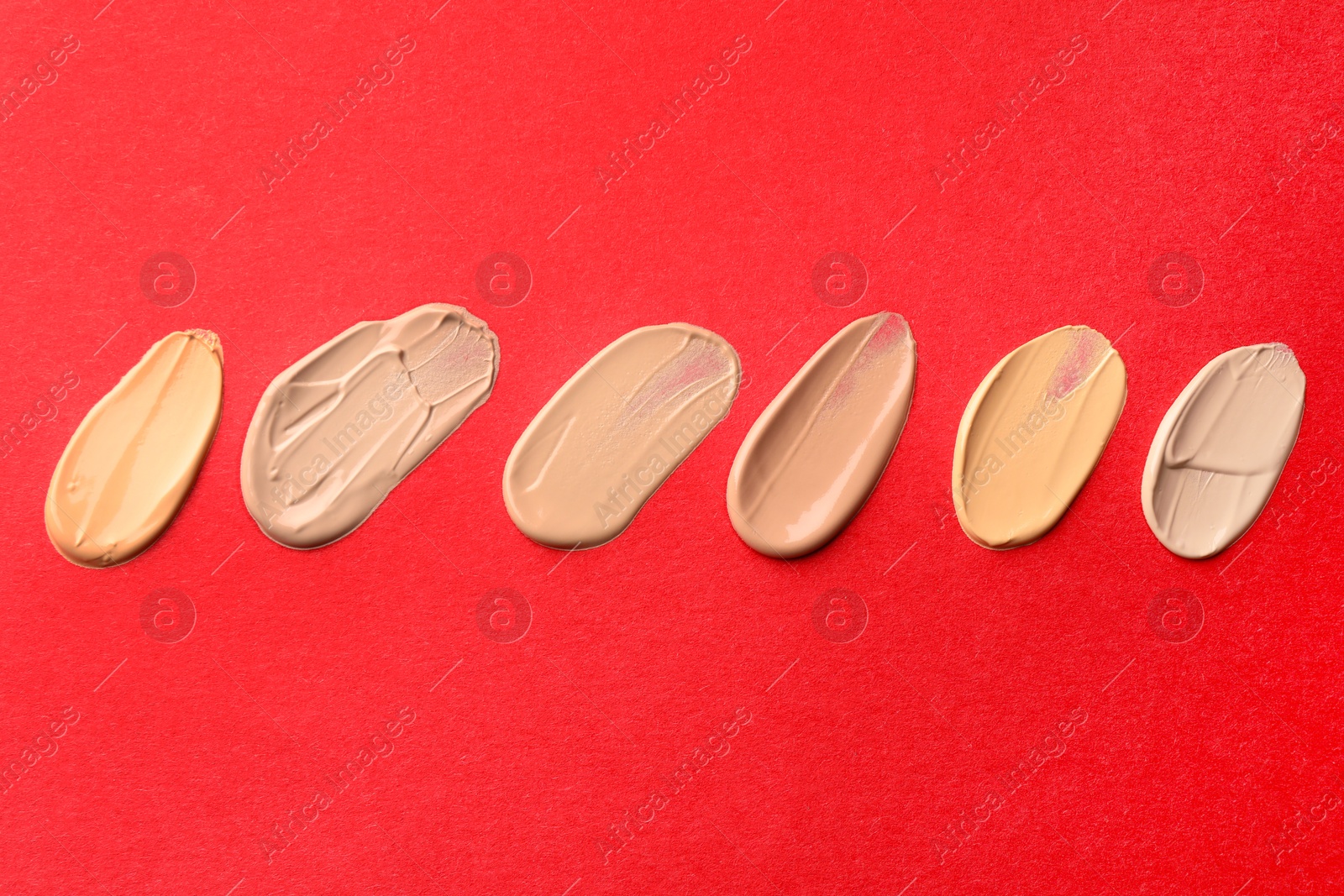 Photo of Samples of different foundations on red background, above view