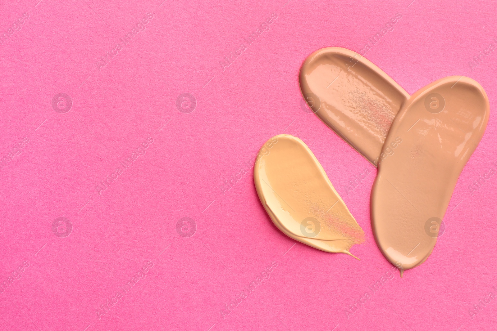 Photo of Foundation on pink background, top view with space for text. Smears of cosmetic product