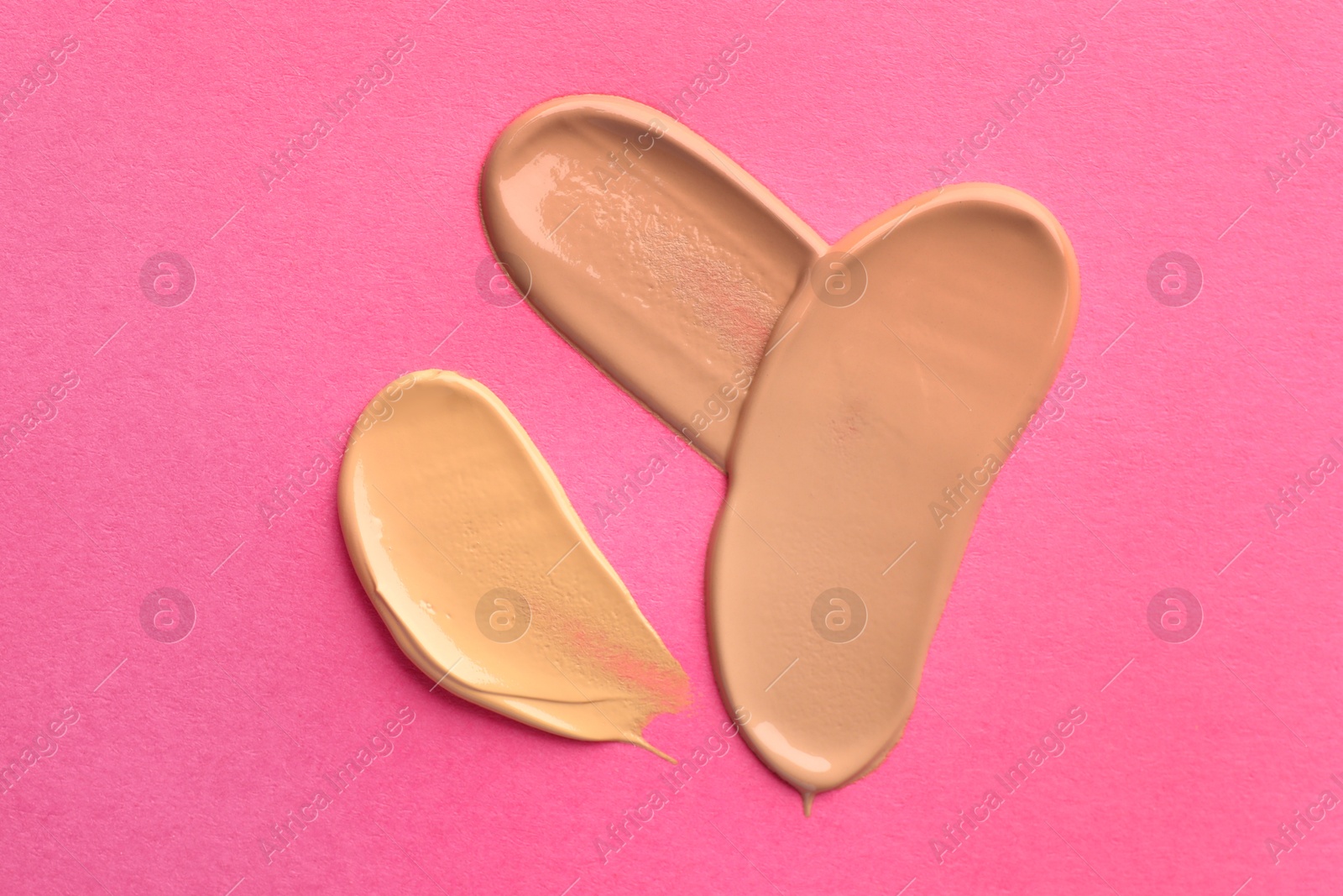 Photo of Foundation on pink background, top view. Smears of cosmetic product