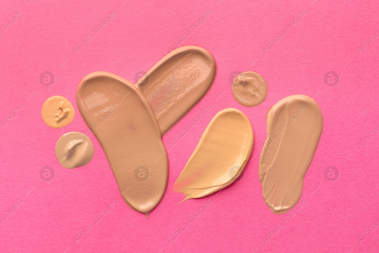 Photo of Foundation on pink background, top view. Smears of cosmetic product