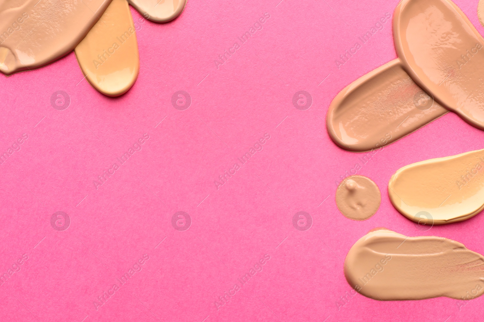 Photo of Foundation on pink background, top view with space for text. Smears of cosmetic product