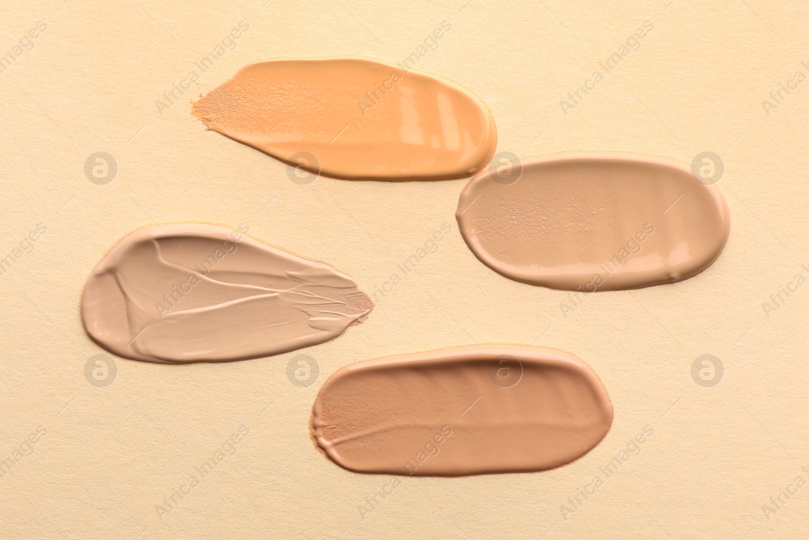 Photo of Samples of different foundations on beige background, top view