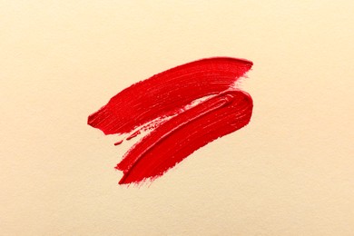 Photo of Red lipstick on beige background, top view. Smears of cosmetic product