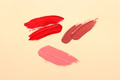 Photo of Different lipsticks on beige background, top view. Smears of cosmetic products