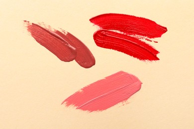 Photo of Different lipsticks on beige background, top view. Smears of cosmetic products