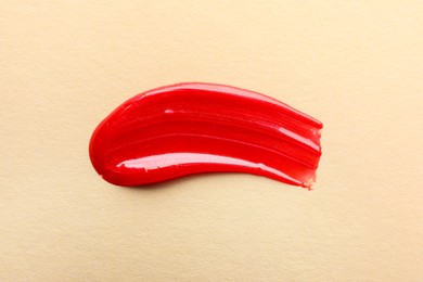 Photo of Red lipgloss on beige background, top view. Smear of cosmetic product