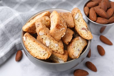 Photo of Tasty almond biscuits (Cantuccini) in bowl and nuts on light table, closeup