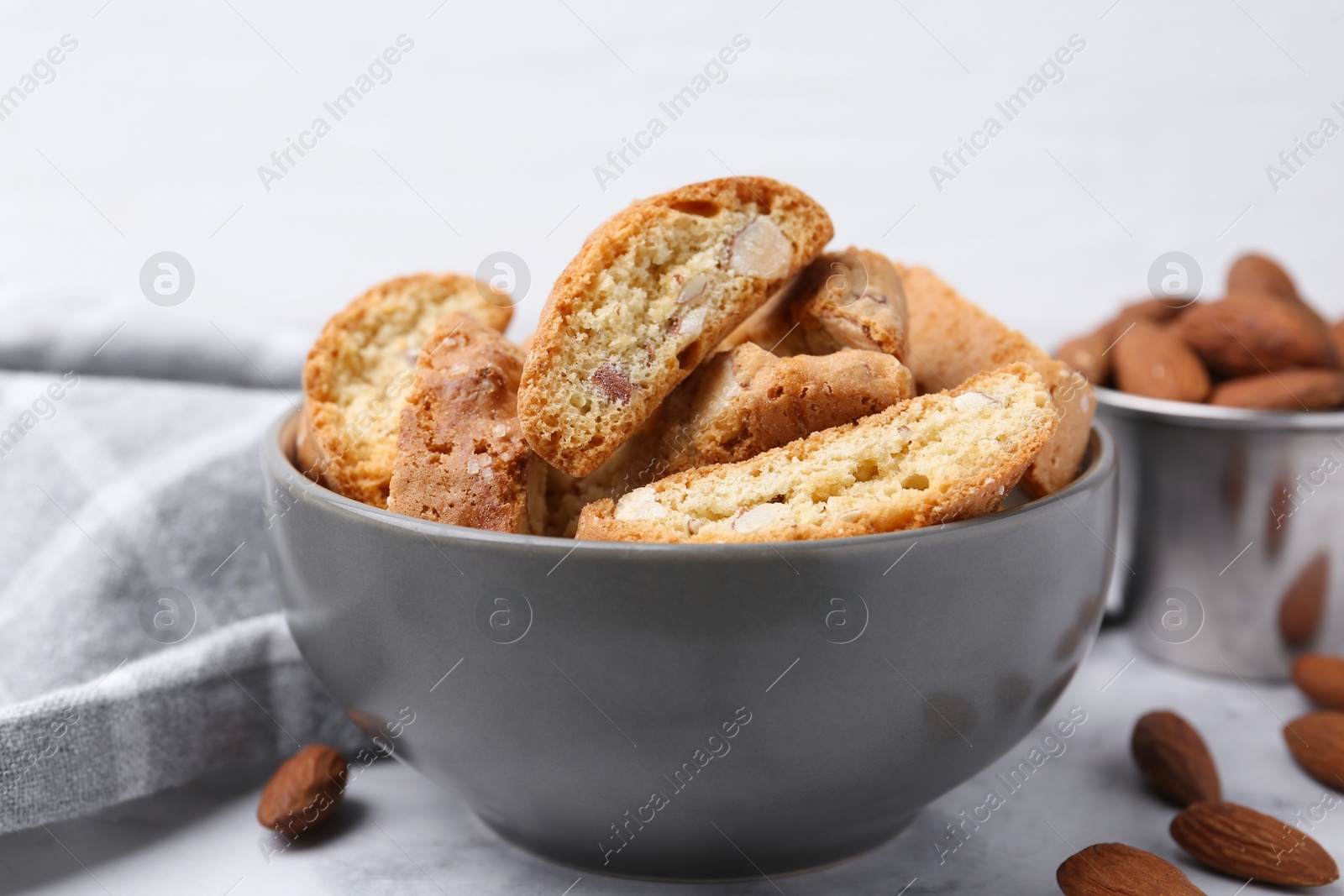 Photo of Tasty almond biscuits (Cantuccini) in bowl and nuts on light table, closeup