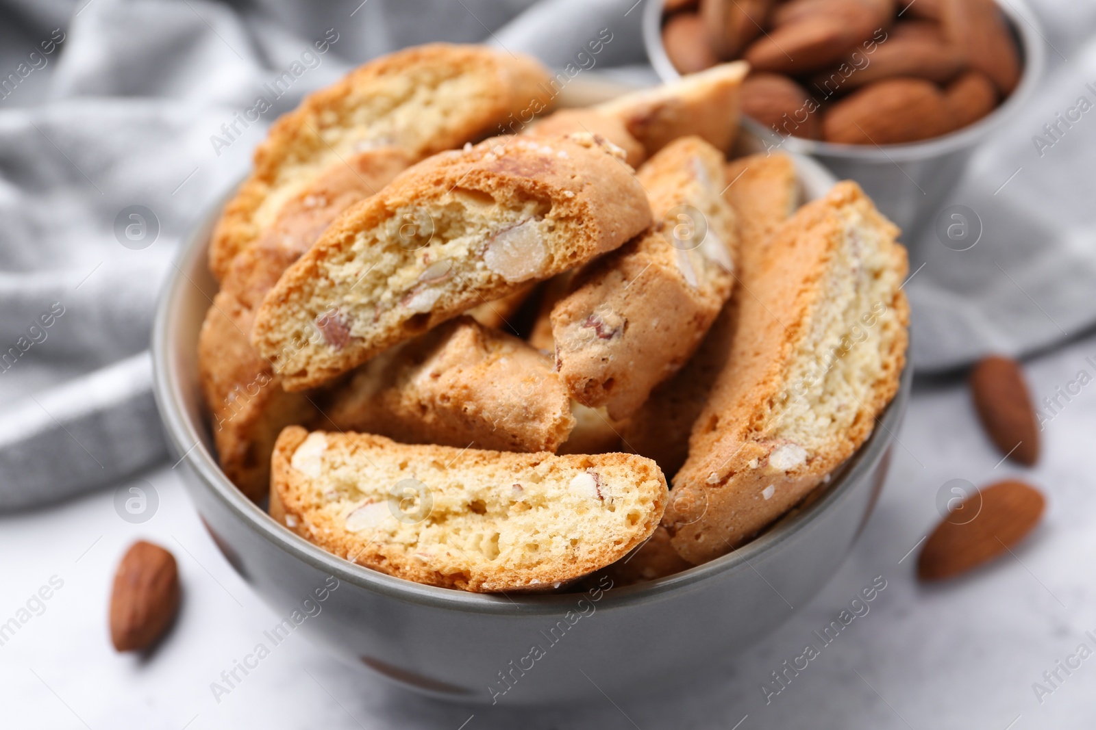 Photo of Tasty almond biscuits (Cantuccini) in bowl and nuts on light table, closeup