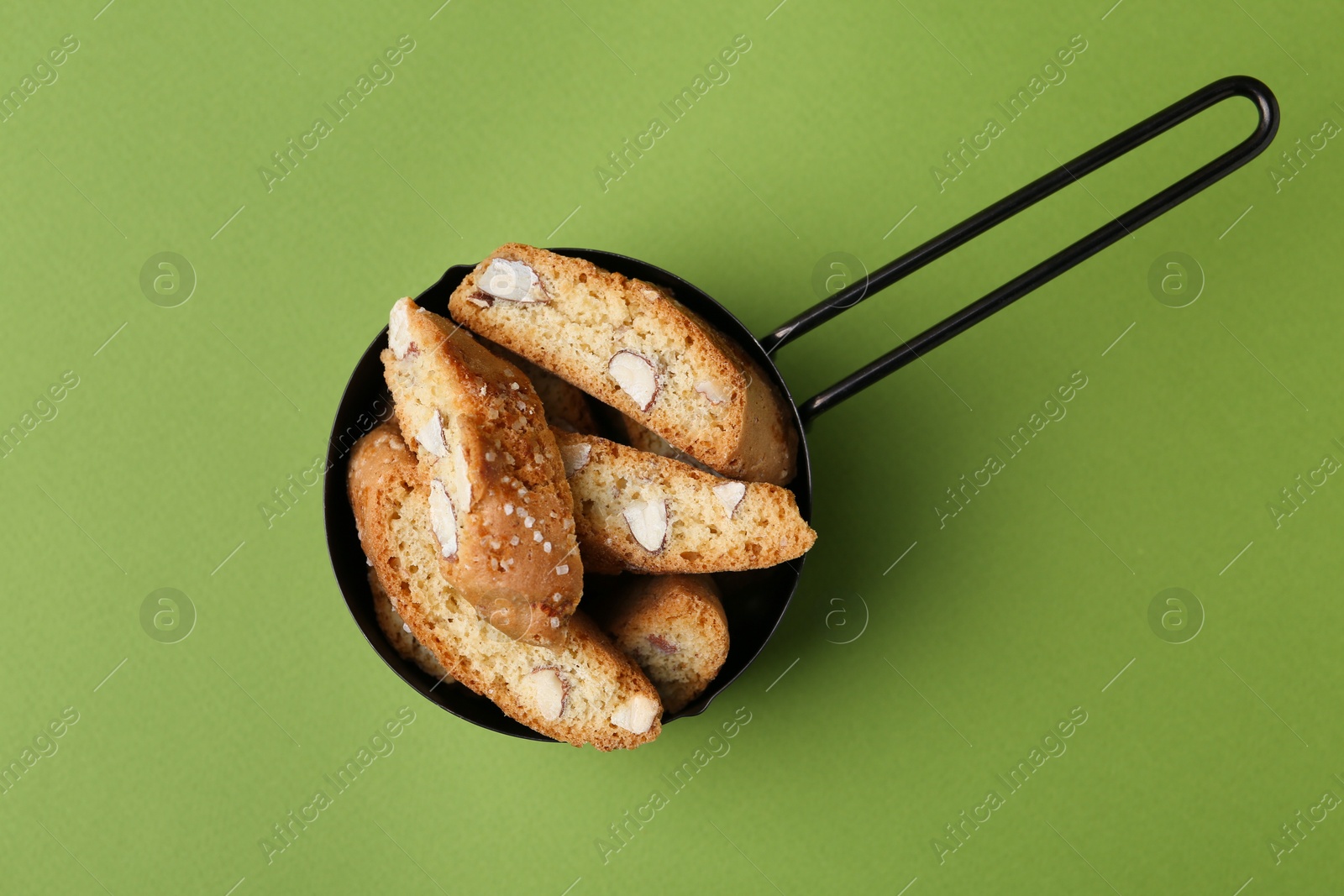 Photo of Tasty almond biscuits (Cantuccini) in scoop on green background, top view