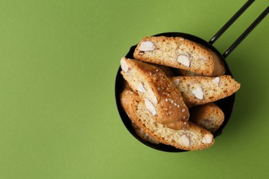 Photo of Tasty almond biscuits (Cantuccini) in scoop on green background, top view. Space for text