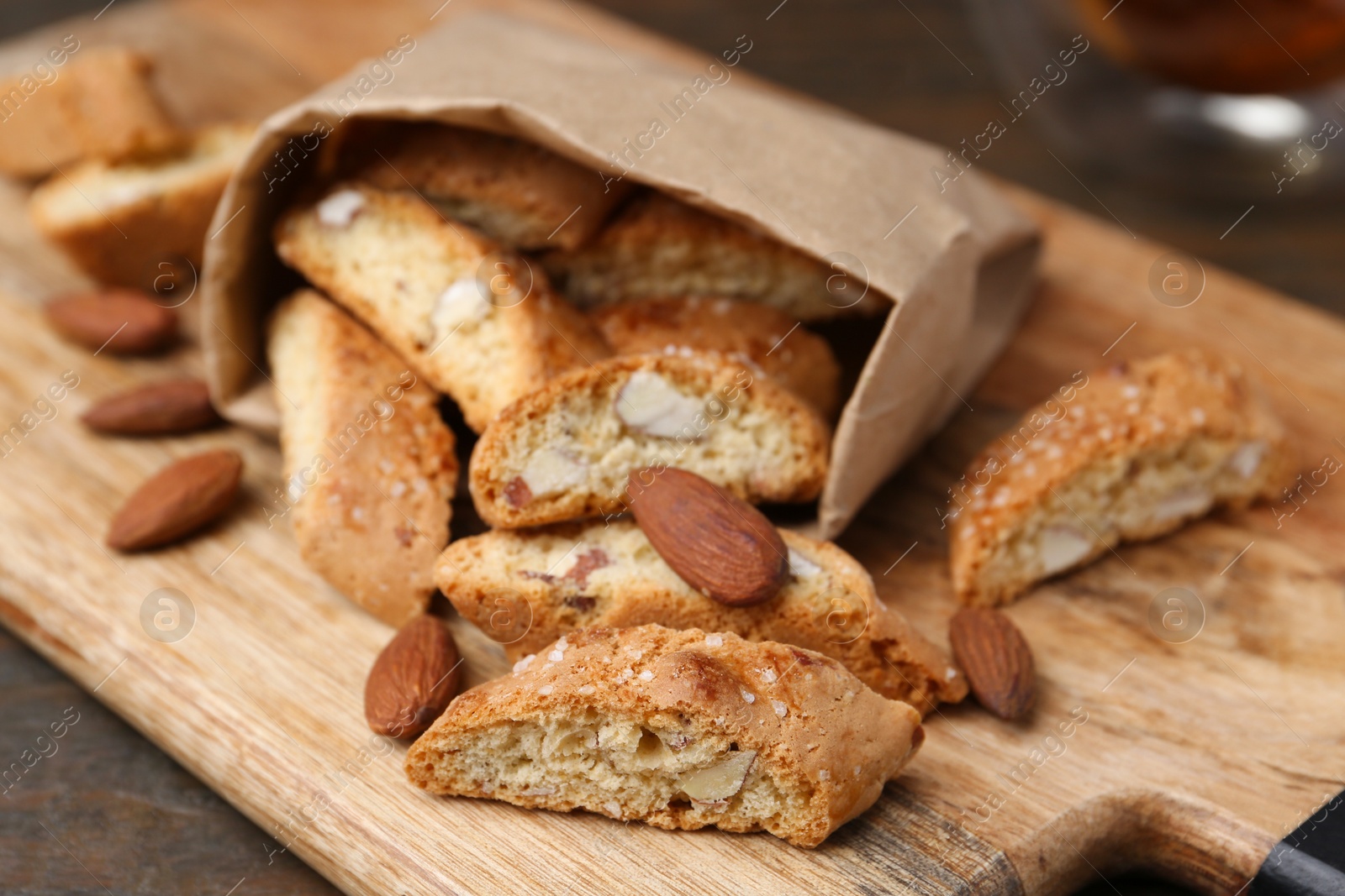 Photo of Paper bag with tasty almond biscuits (Cantuccini) and nuts on wooden table, closeup