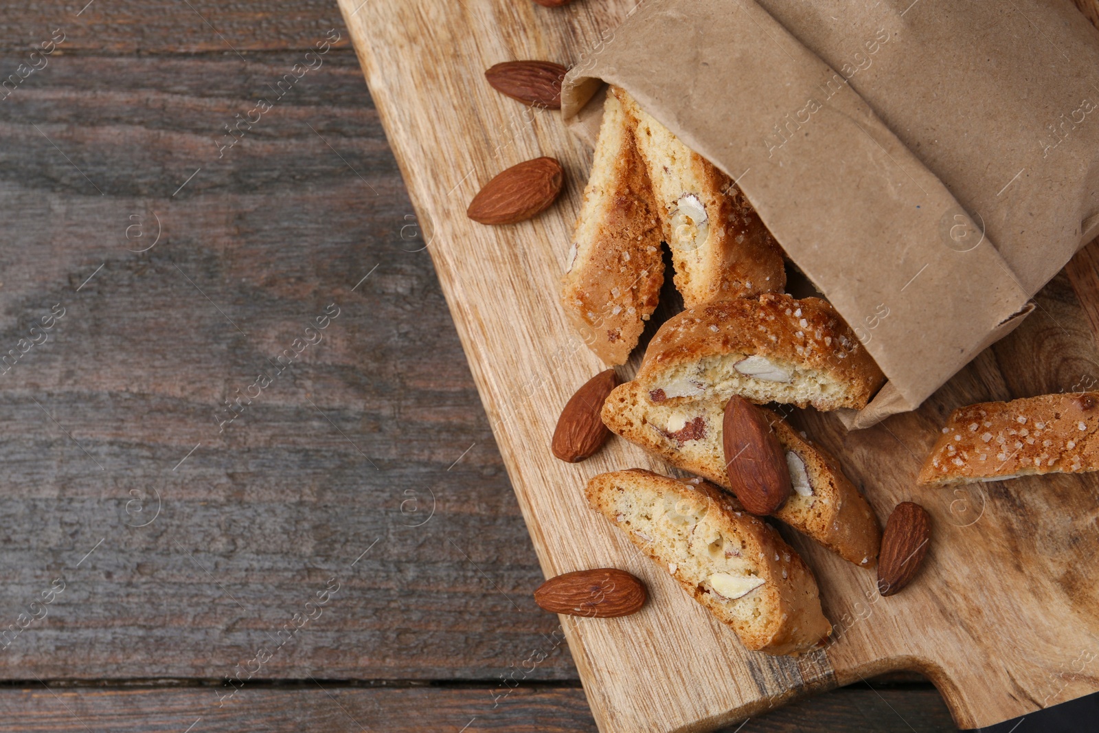 Photo of Paper bag with tasty almond biscuits (Cantuccini) and nuts on wooden table, top view. Space for text