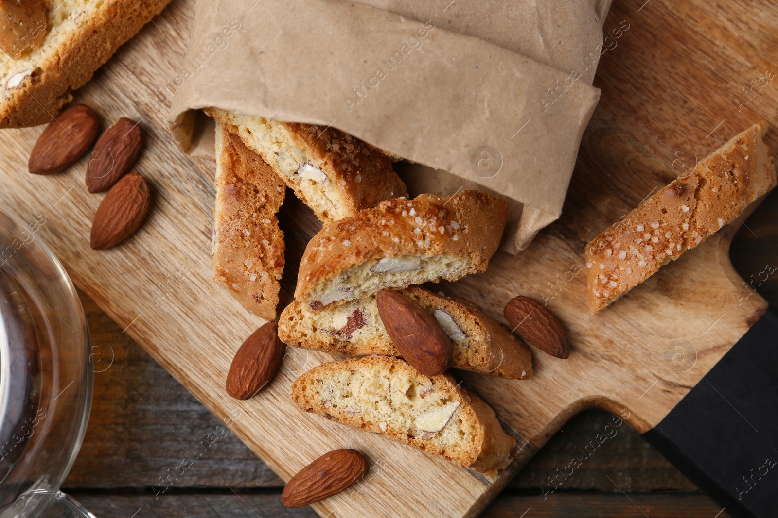 Photo of Paper bag with tasty almond biscuits (Cantuccini) and nuts on wooden table, top view