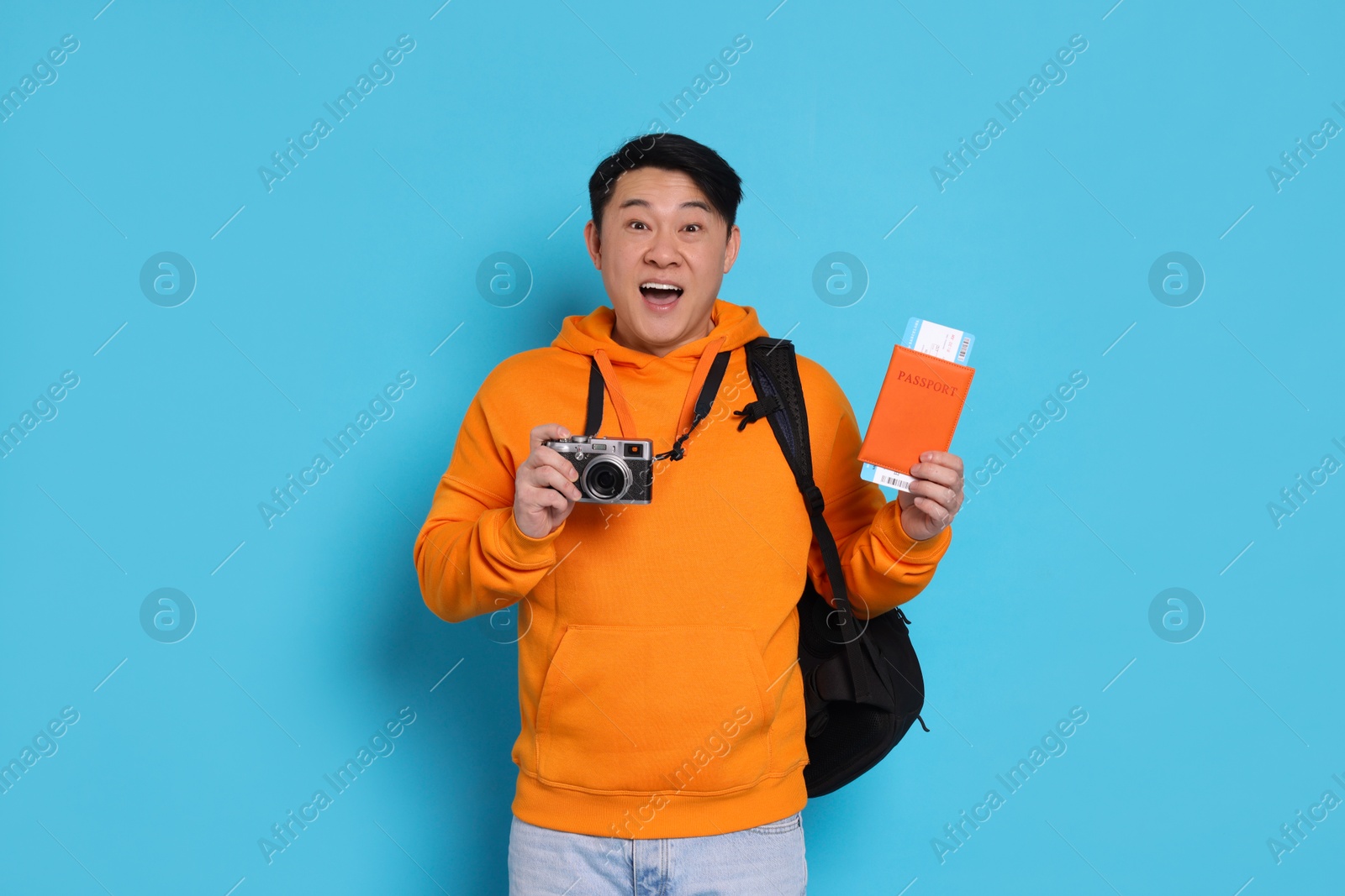 Photo of Excited traveller with passport and camera on light blue background