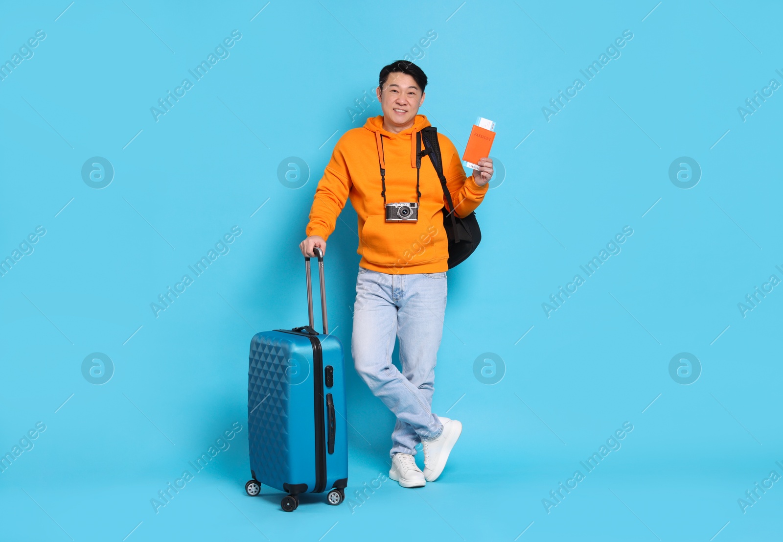 Photo of Happy traveller with passport, suitcase and camera on light blue background