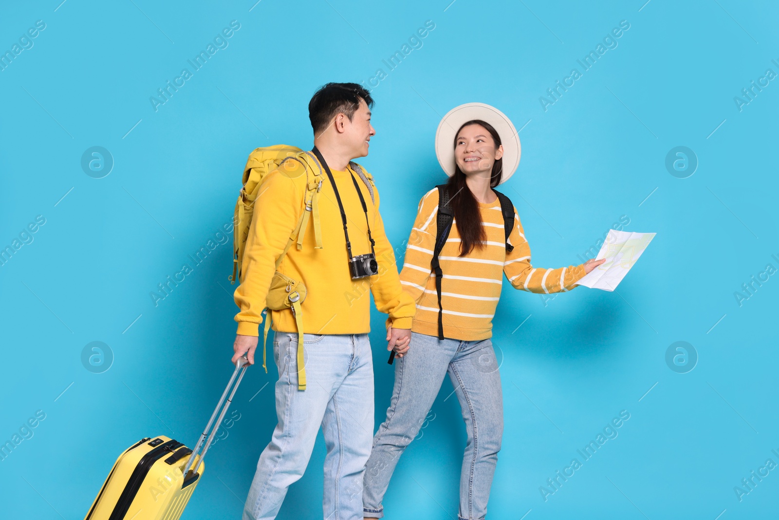 Photo of Happy travellers with suitcase and map on light blue background