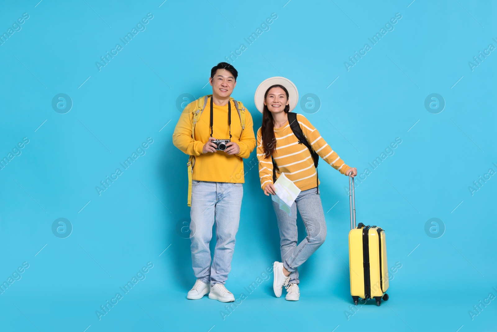 Photo of Happy travellers with suitcase and map on light blue background