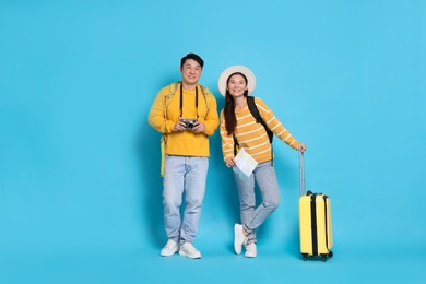 Happy travellers with suitcase and map on light blue background