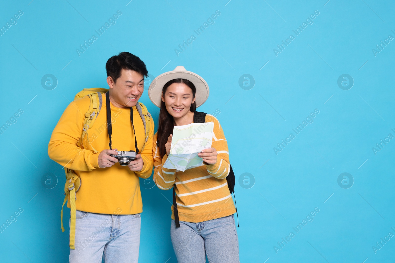 Photo of Happy travellers with camera and map on light blue background. Space for text