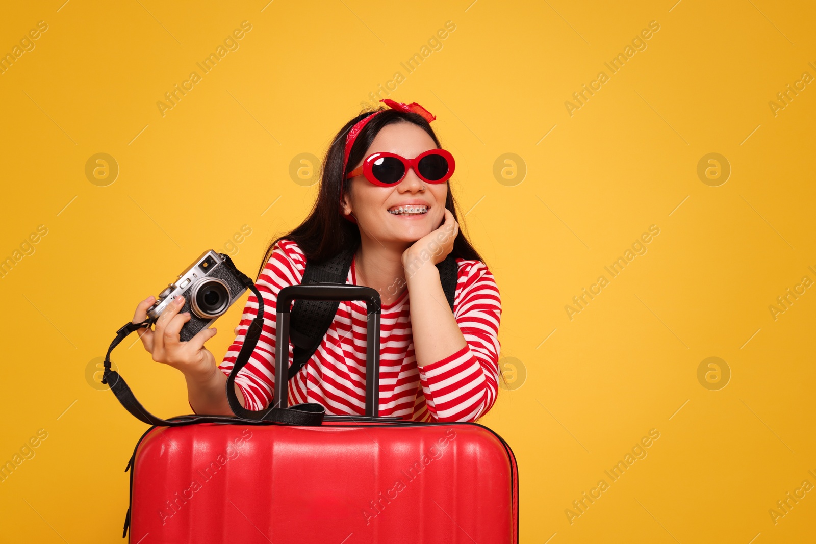 Photo of Happy traveller with camera and suitcase on yellow background. Space for text