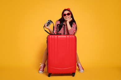 Photo of Happy traveller with camera and suitcase on yellow background