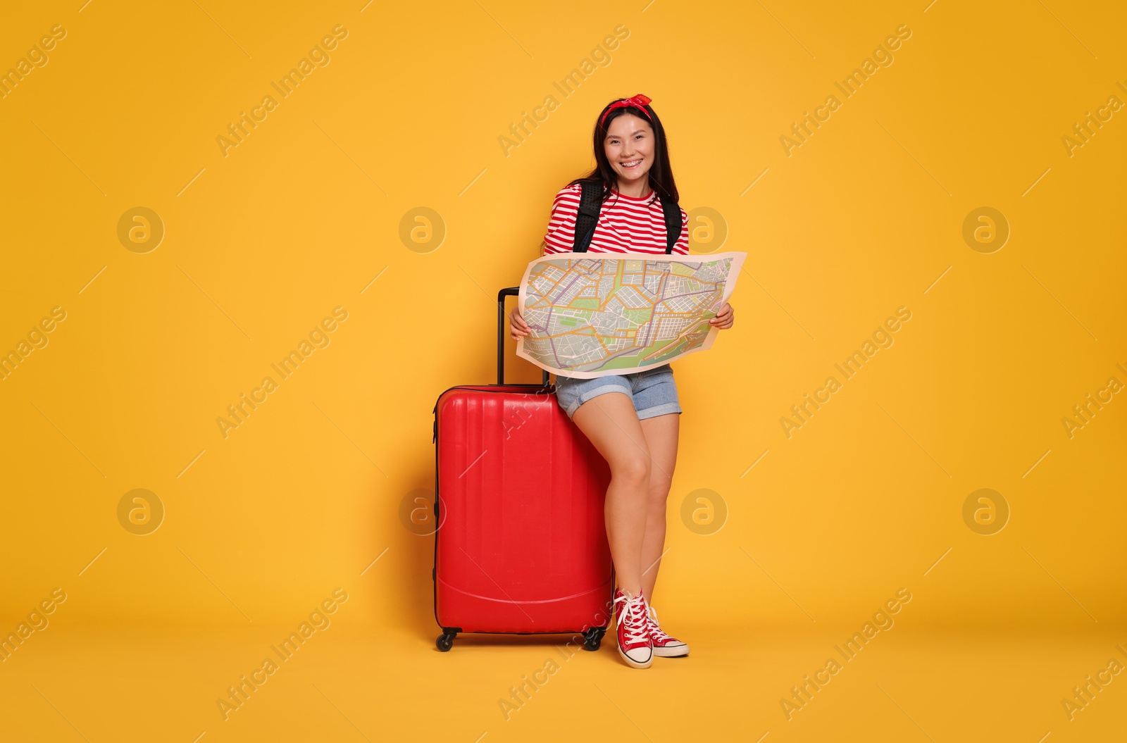 Photo of Happy traveller with map and suitcase on yellow background