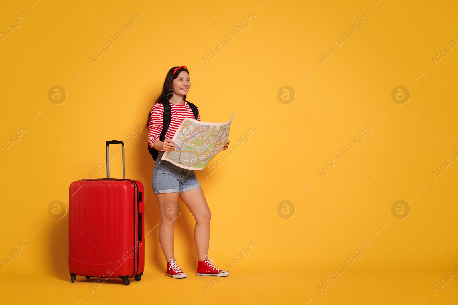 Photo of Happy traveller with map and suitcase on yellow background. Space for text