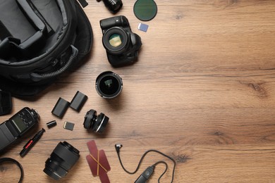 Photo of Professional photographer's equipment and backpack on wooden background, flat lay. Space for text