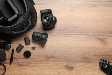 Photo of Professional photographer's equipment and backpack on wooden background, flat lay. Space for text