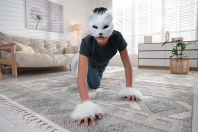 Photo of Quadrobics. Boy wearing cat mask, gloves and tail on floor at home